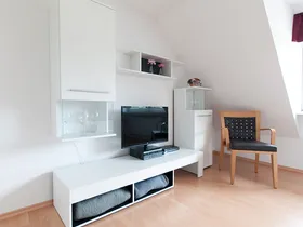 Wohnbereich mit Fernseher, Sideboard und Sessel unter der Dachschräge